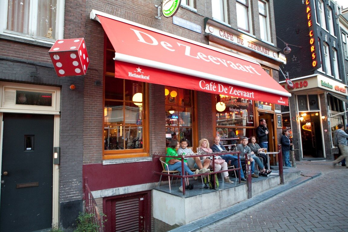 De gevel van Café de Zeevaart met de rode luifel en het terras