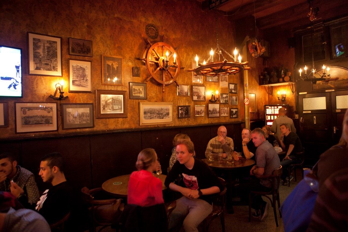 Interieur van Café de Zeevaart met houten lambrisering, ingelijste platen en een stuurwiel